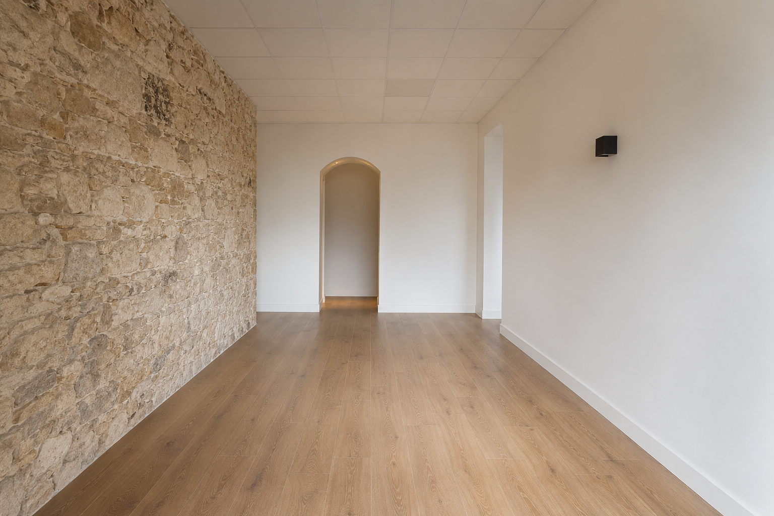 Vue intérieure du studio LOUMA, espace ouvert entre mur de pierre apparente et mur blanc lisse, arche en fond